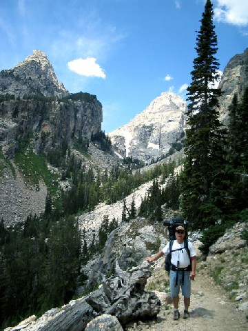 Andrew standing on the trail with rocky mountains around and behind him.