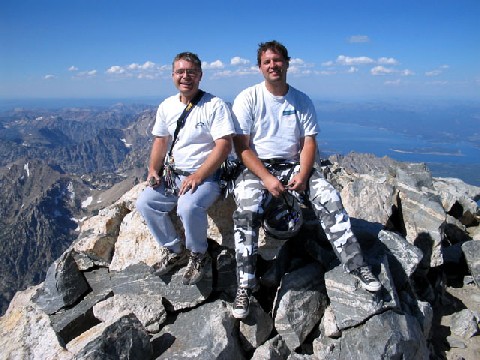 Andrew and Jeff sitting at the top of the mountain with a beautiful view of other mountains and valley behind them.