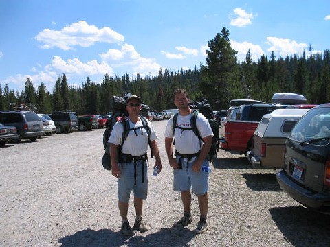 Andrew and Jeff with their backpacks on standing in the parking lot by the cars after finishing their hike.